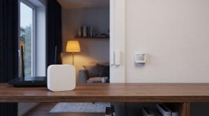 Unbranded white smart home hub on a wooden shelf beside a Wi-Fi router, door sensor and motion sensor at dusk